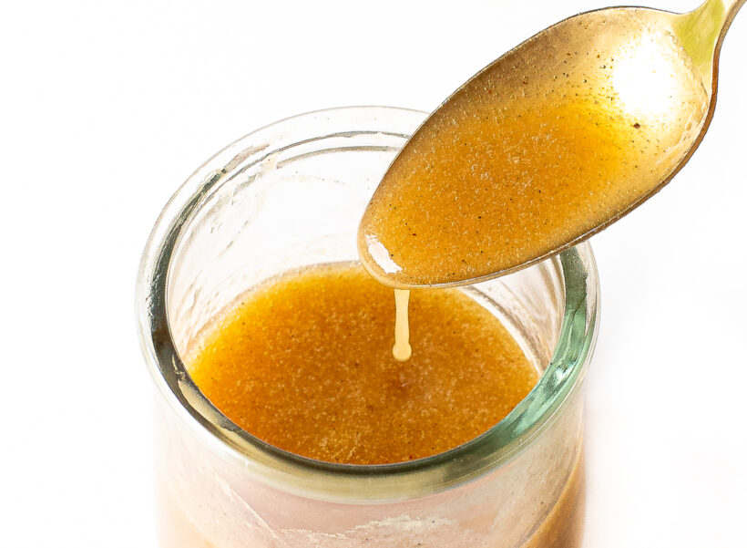 Banana bread syrup in a glass jar with a spoon drizzling some of the syrup.