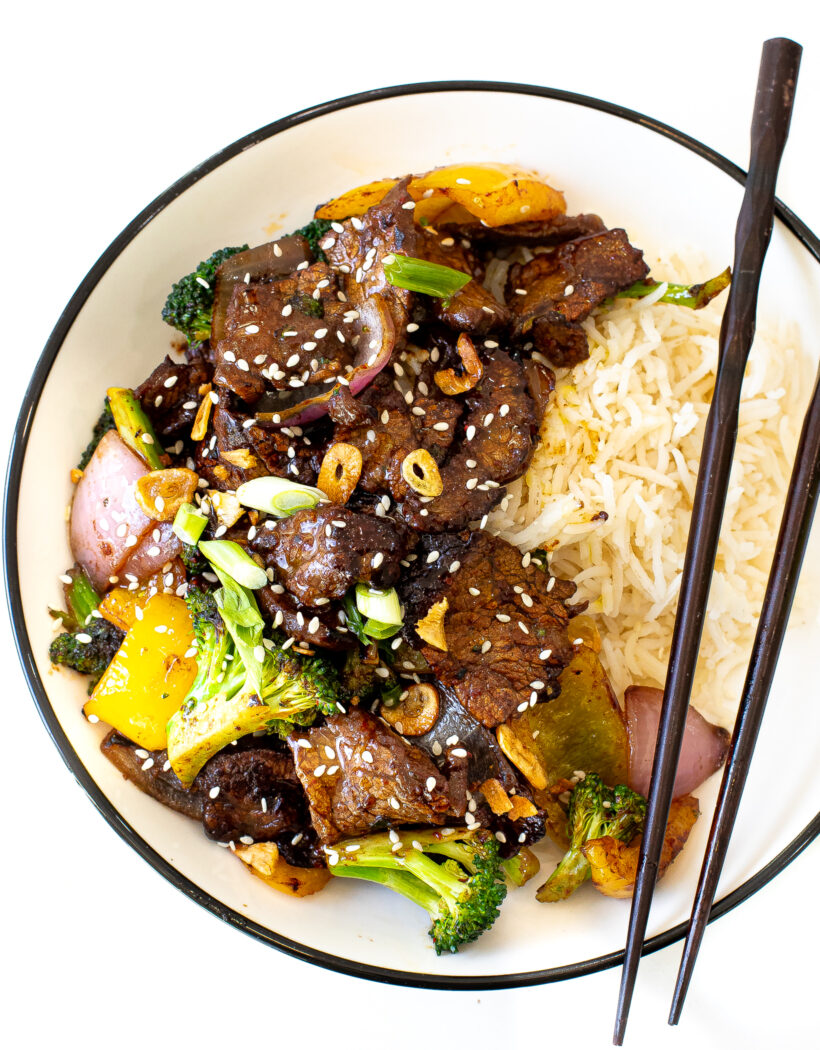 Beef Stir Fry and rice in a white bowl with black chopsticks laying across the bowl.