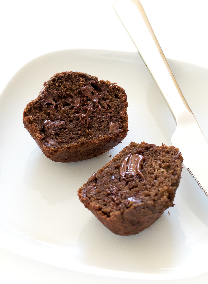 Easy Chocolate Muffins | chefsavvy.com Double Chocolate Chip Muffins on a white plate sliced open with a butter knife.