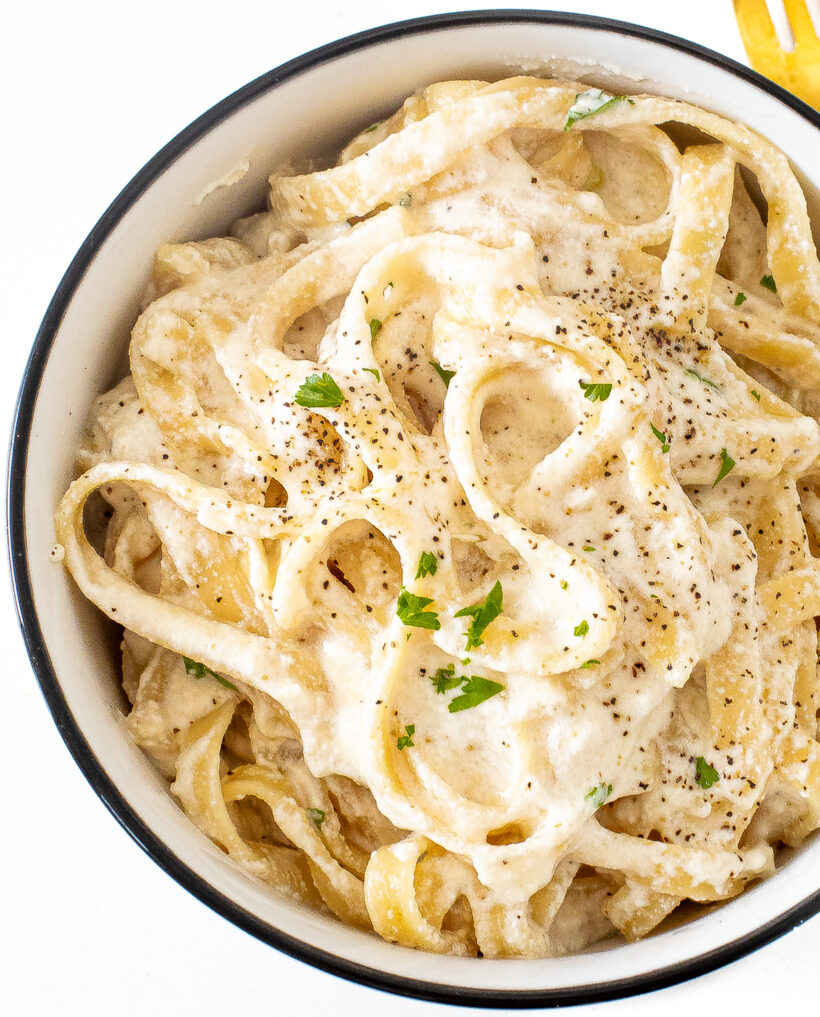 A top down view of cottage cheese alfredo in a white bowl topped with pepper and parsley.