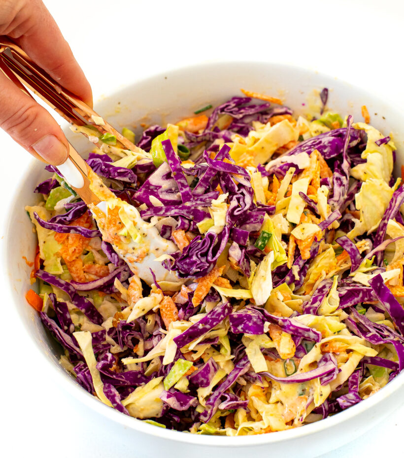 Hand holding a pair of tongs in a large bowl of coleslaw.