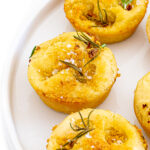 Focaccia muffins topped with salt and rosemary served on a white plate.