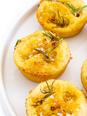 Focaccia muffins topped with salt and rosemary served on a white plate.