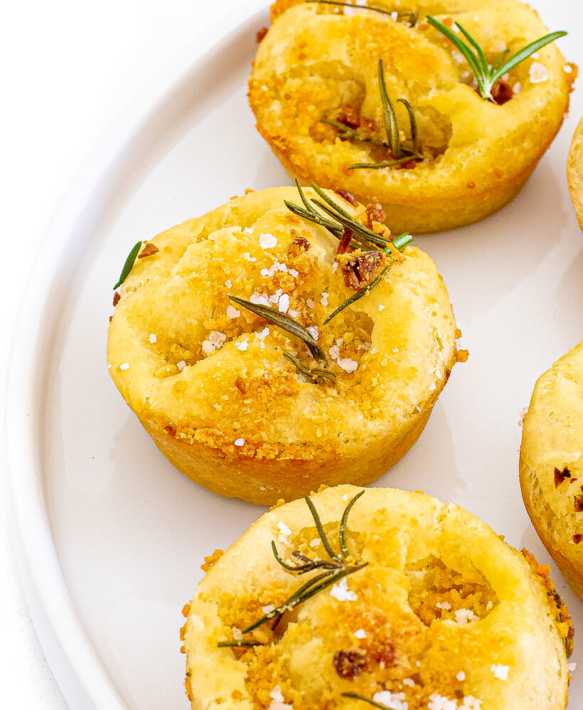 Focaccia muffins served on a white plate topped with rosemary and salt.