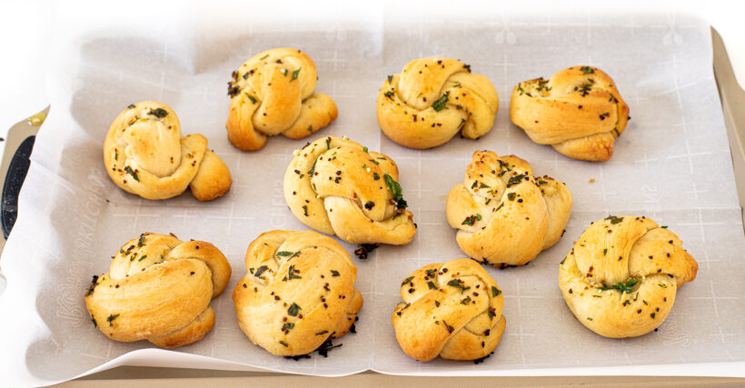 Garlic knots on a baking sheet lined with parchment paper after being baked.