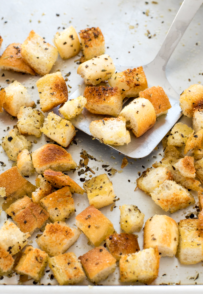 croutons on a baking sheet being scooped up with a metal spatula 