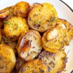 Melting potatoes sliced into rounds, roasted with herbs and garlic on a white plate.