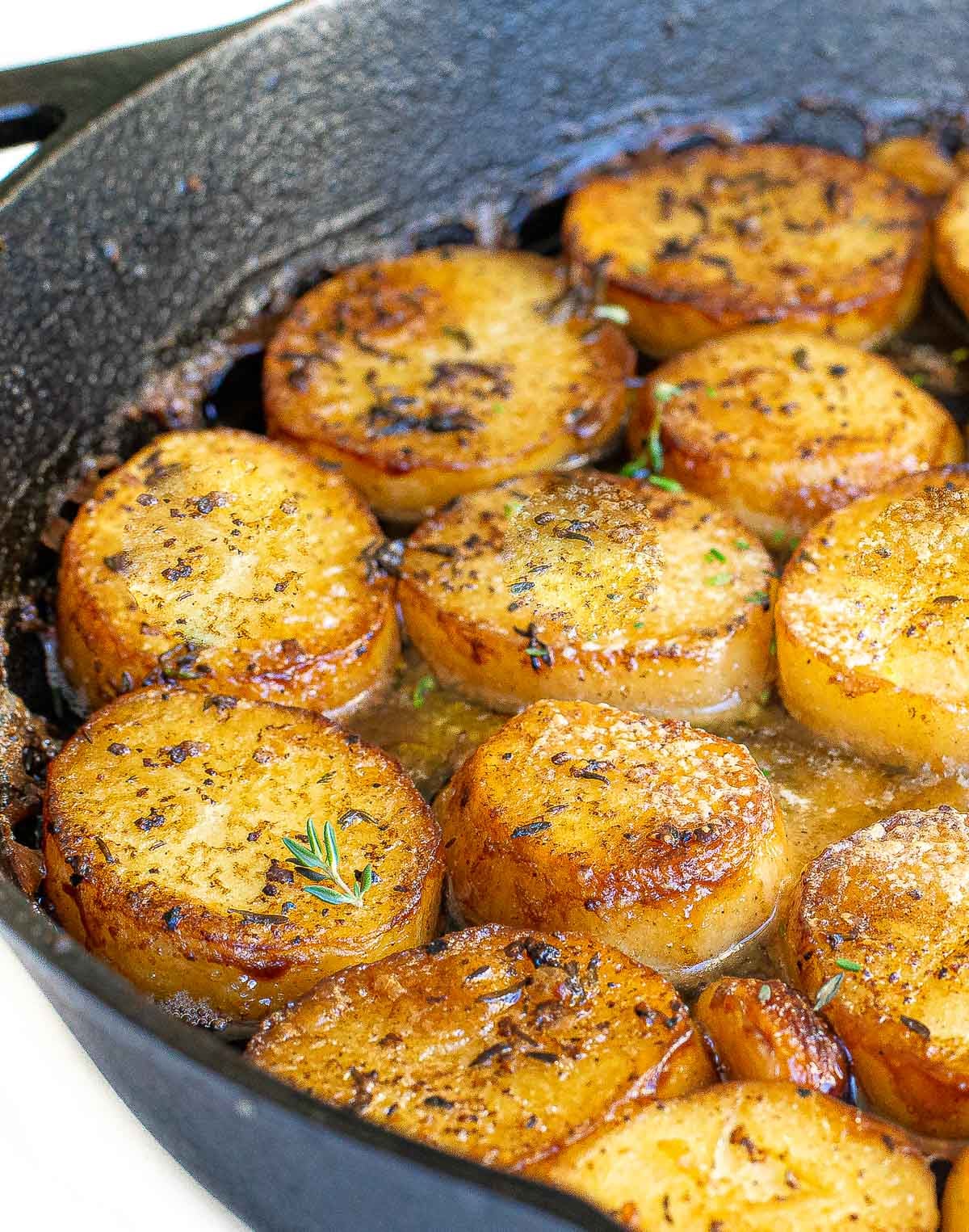 Golden-brown melting potatoes pan-seared with herbs in a cast-iron skillet.