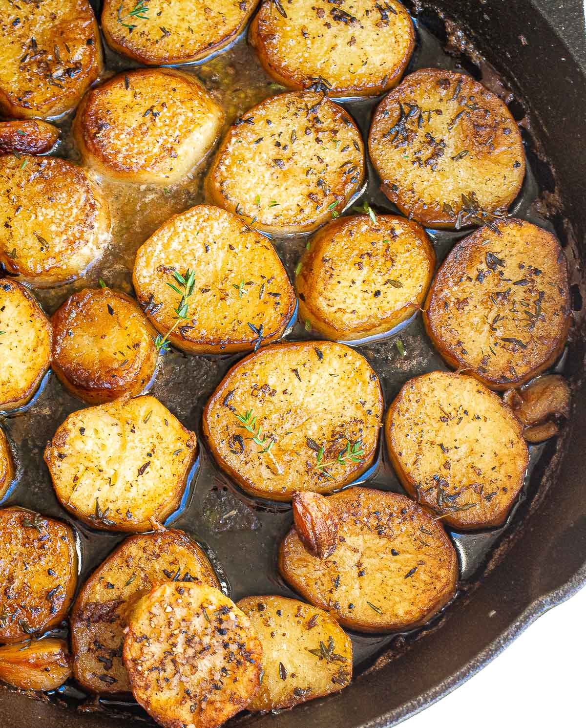 Pan-seared melting potatoes seasoned with herbs in a cast-iron skillet.