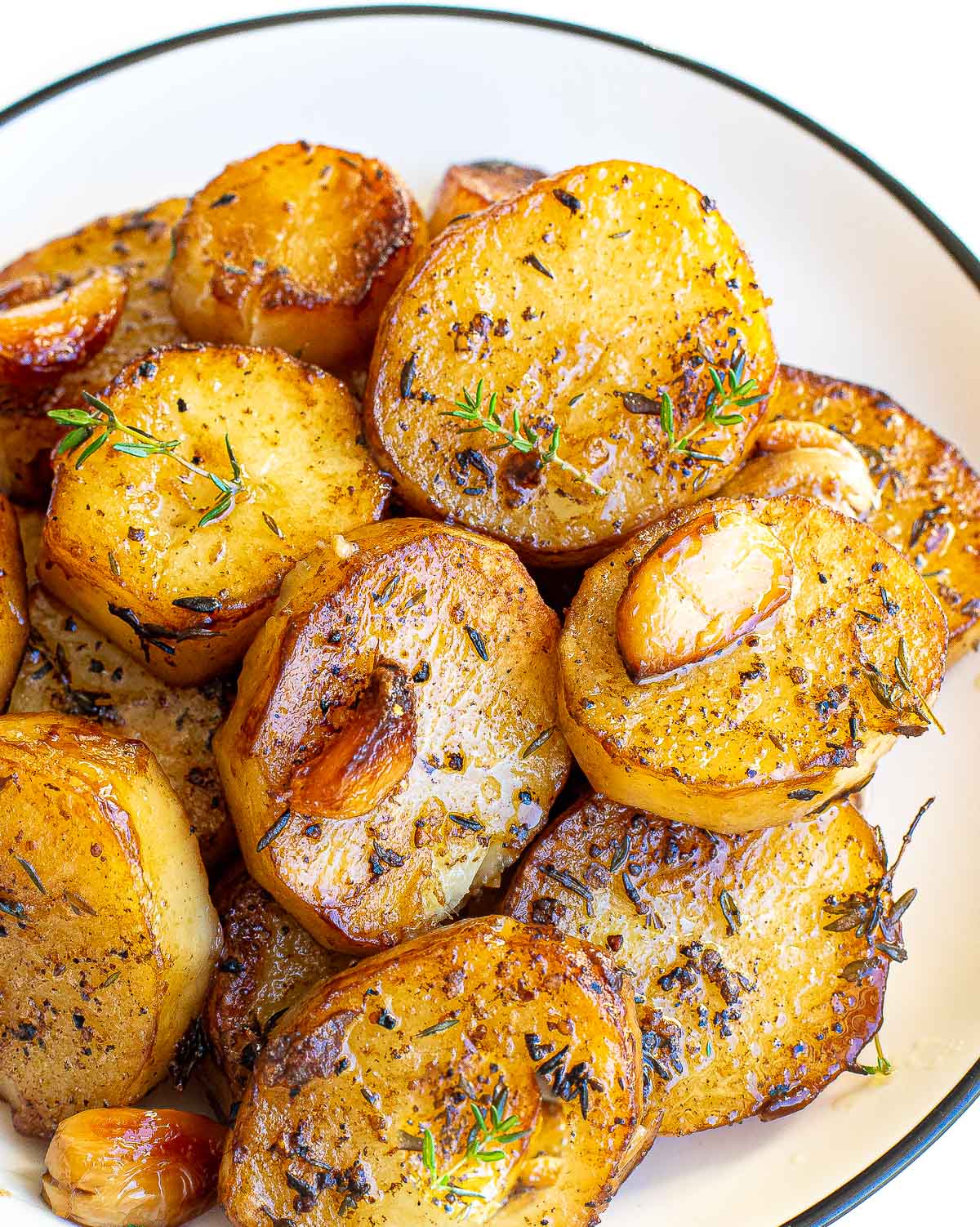 Melting potatoes sliced into rounds, roasted with herbs and garlic on a white plate.