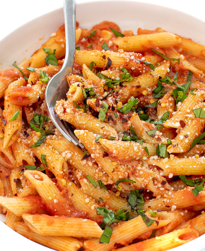 Penne noodles with tomato sauce in a white bowl with a fork. 