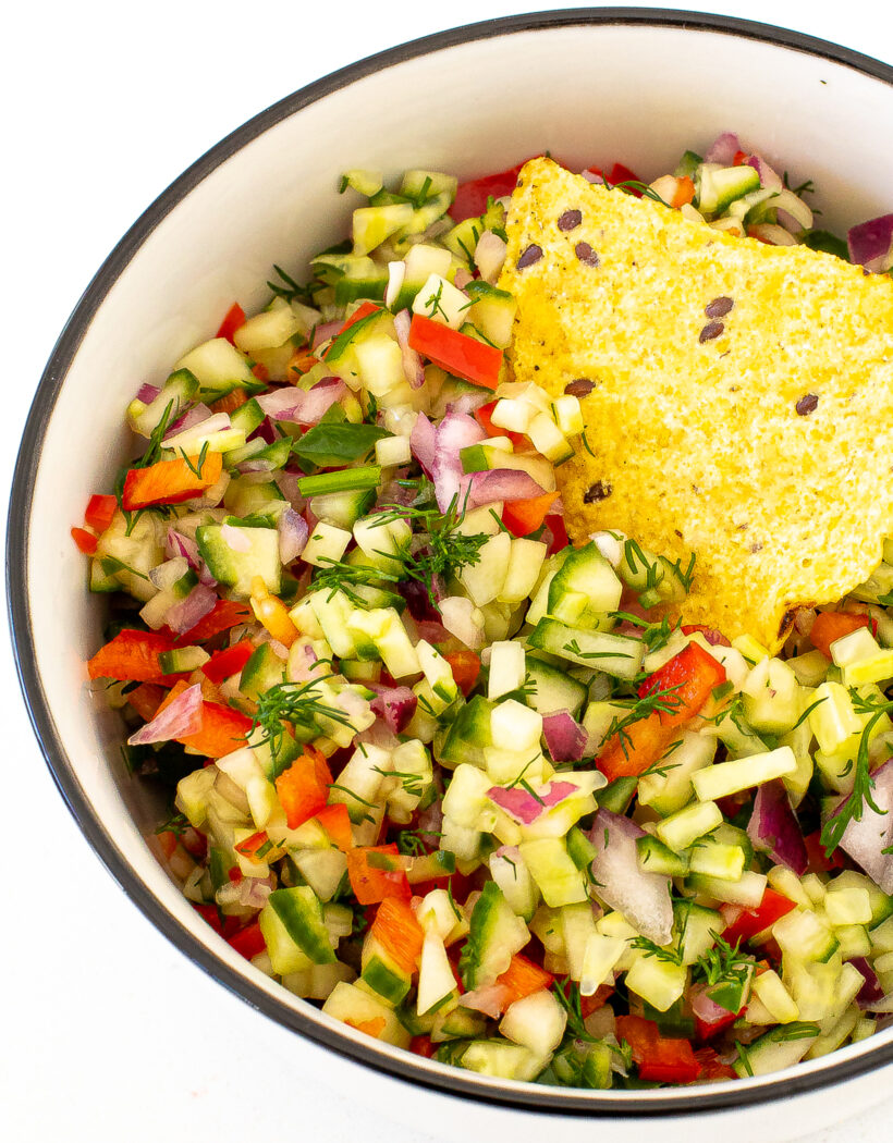 Pickle de gallo in a black rimmed white serving bowl. A chip is in the dip.