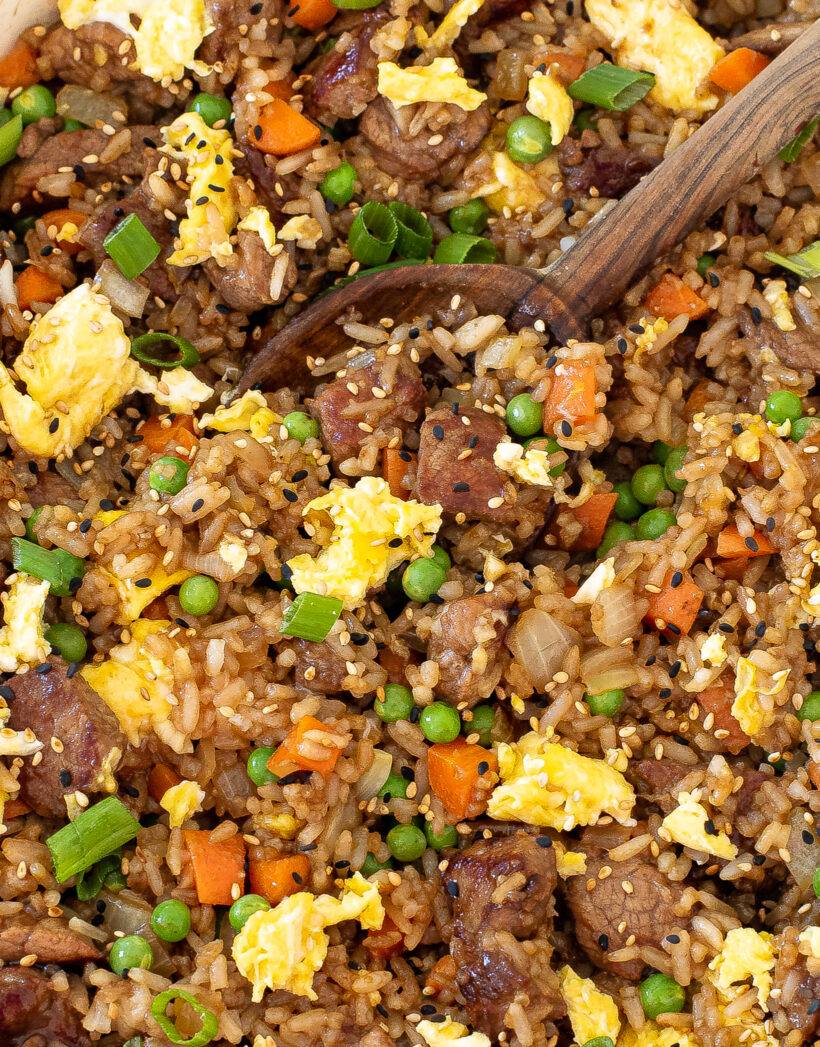 Up close shot of pork fried rice in a skillet with a wooden spoon.