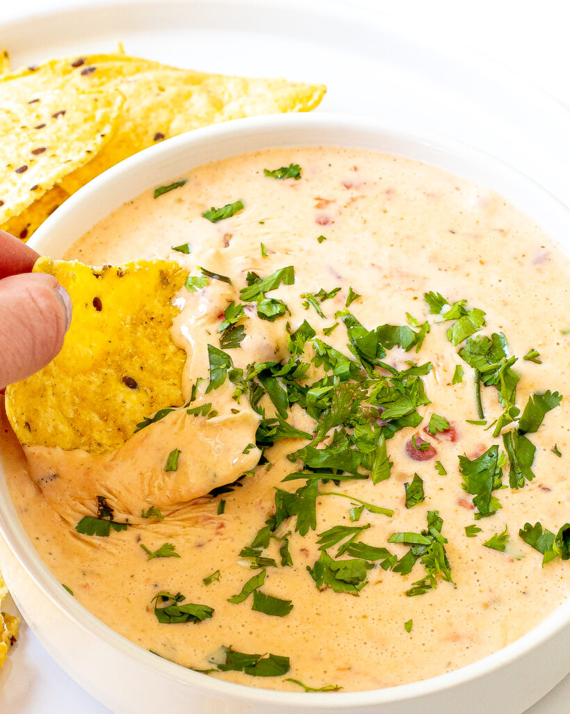 A hand dipping a chip into the bowl of queso.