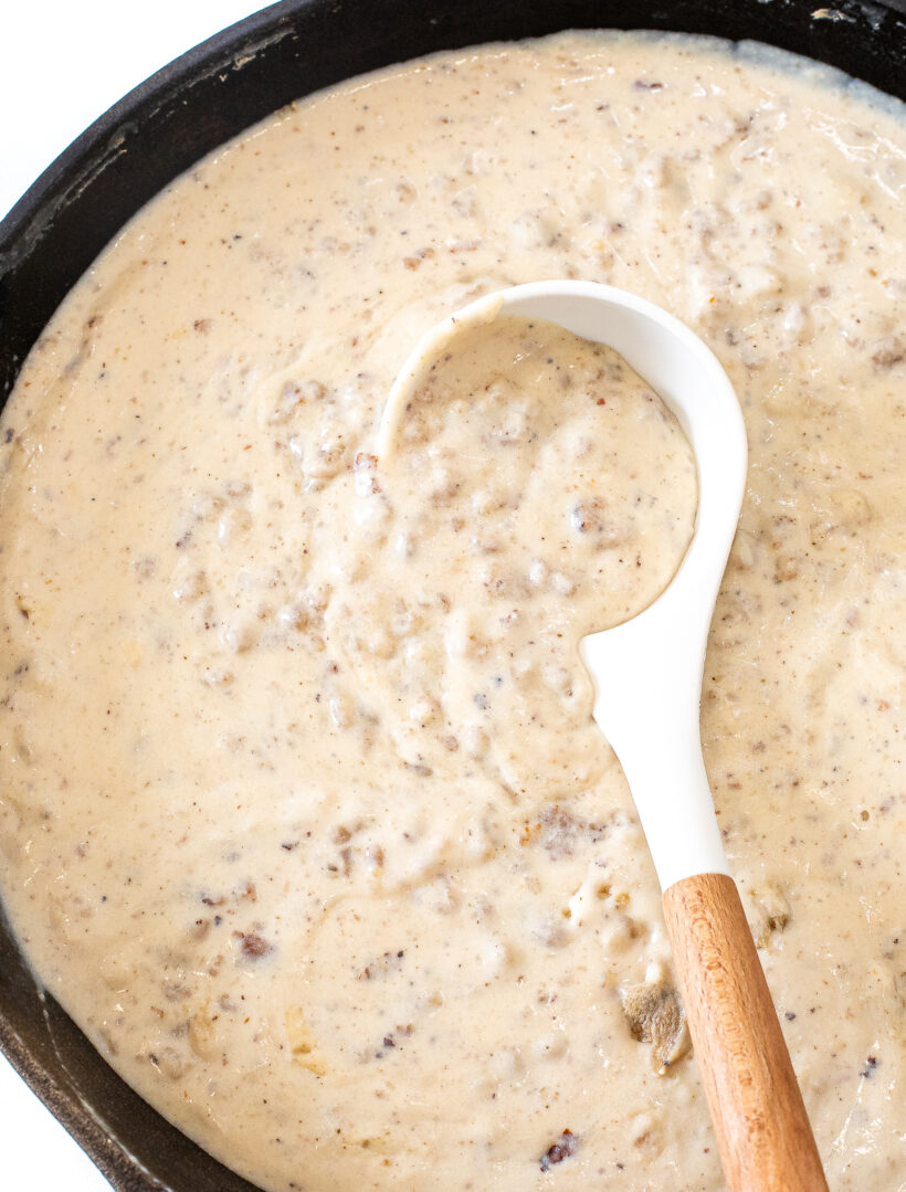 A white and wood spoon in a pan full of sausage gravy.