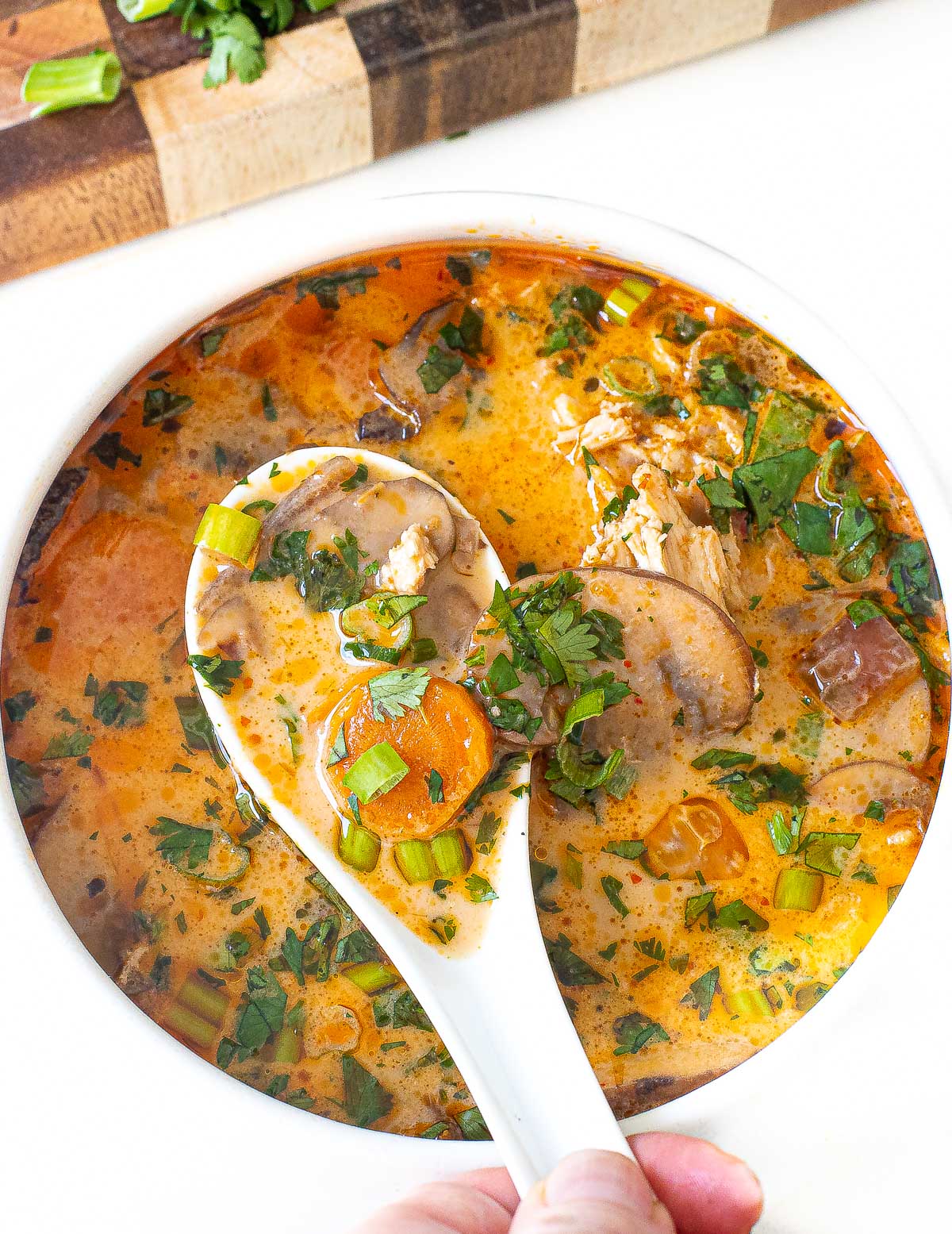 spoon dipped in thai coconut soup with fresh herbs on top