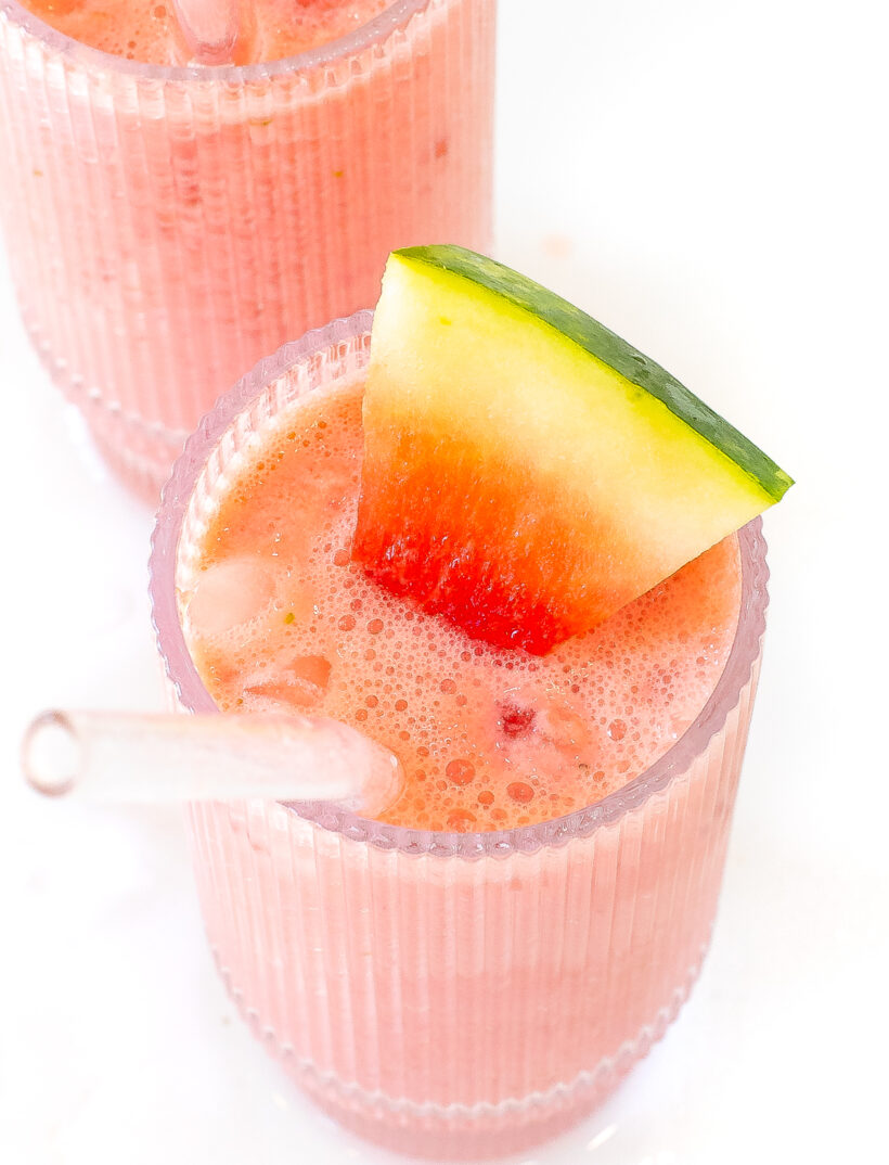 Watermelon smoothie in a glass with a straw and a slice of watermelon on the side.