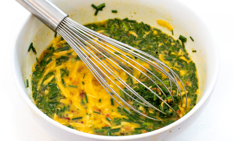 Eggs being whisked with chives, cheese and bacon. 