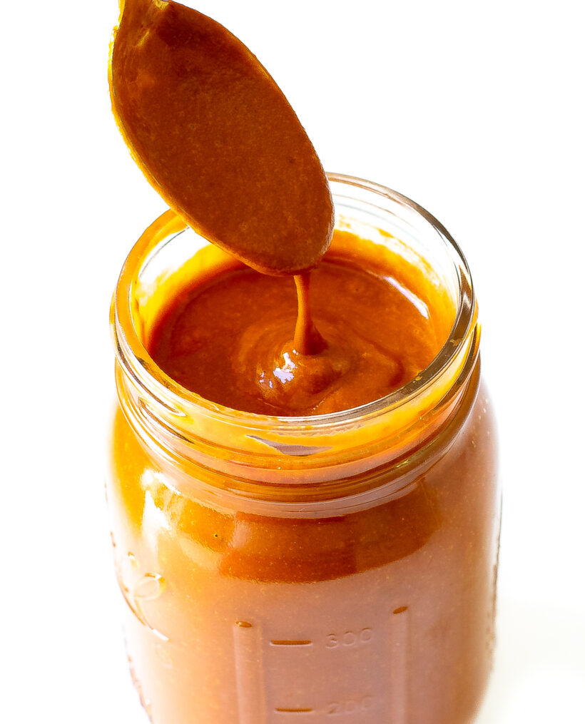 A spoon drizzling enchilada sauce into a glass jar.