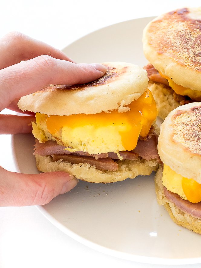author scooping up English muffin sandwich with eggs, cheese and ham