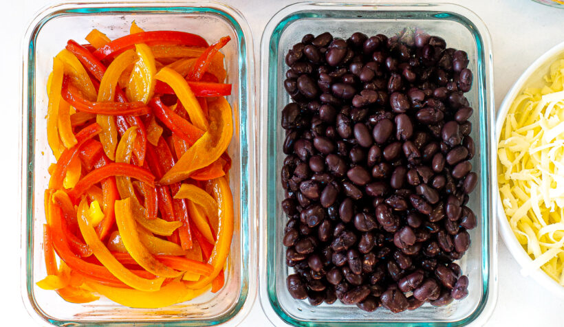 Sauted peppers, black beans, and shredded cheese in glass containers.