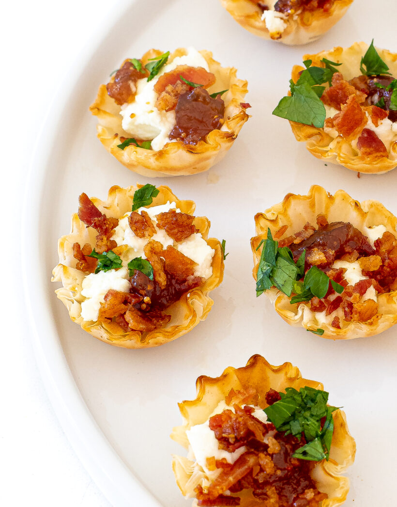 Phyllo cups filled with goat cheese, bacon, fig jam and topped with parsley on a serving platter.