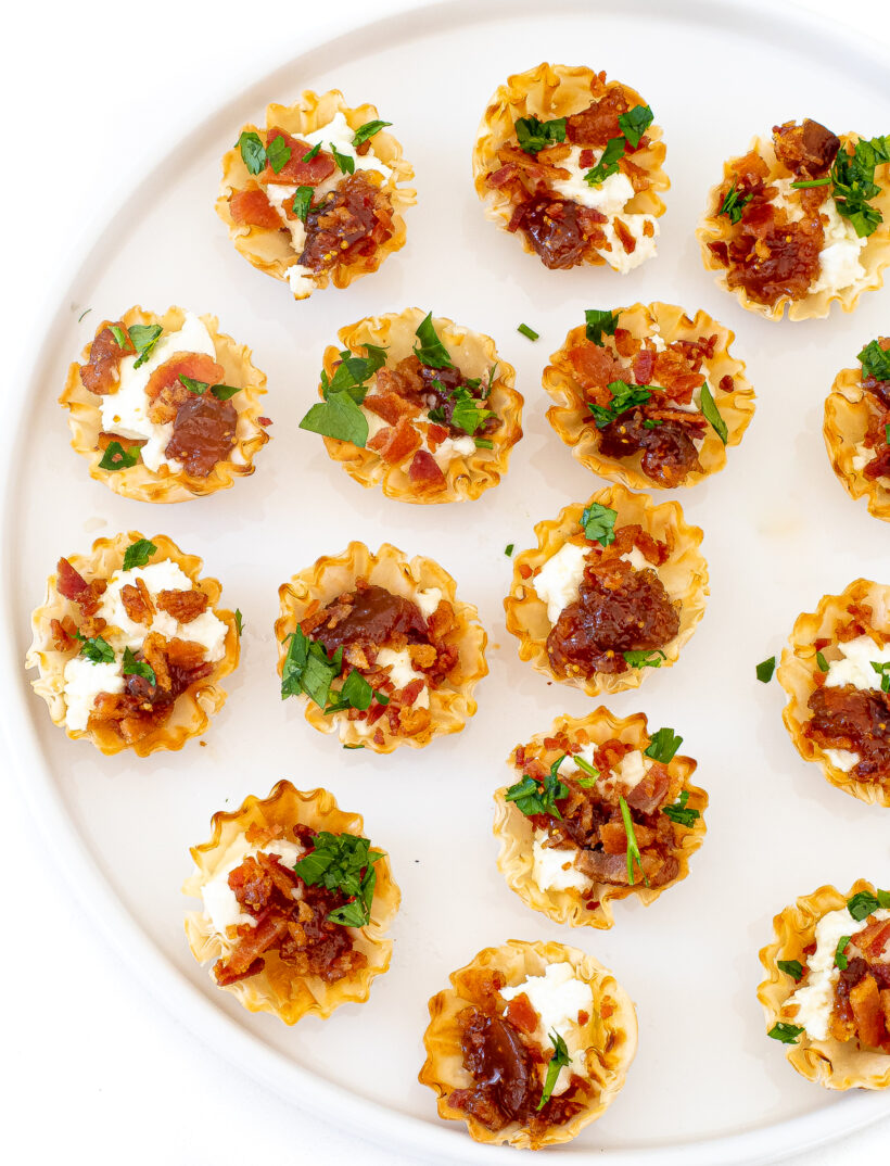 Phyllo cups filled with goat cheese, bacon, fig jam and topped with parsley on a serving platter.