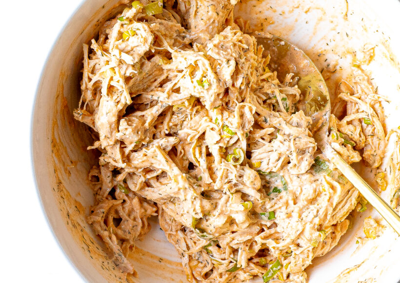 Buffalo chicken filling mixed with a spoon in a white bowl.