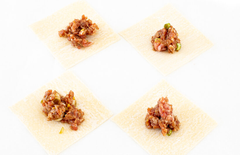 Wonton wrappers laid out with a scoop of filling on each one.