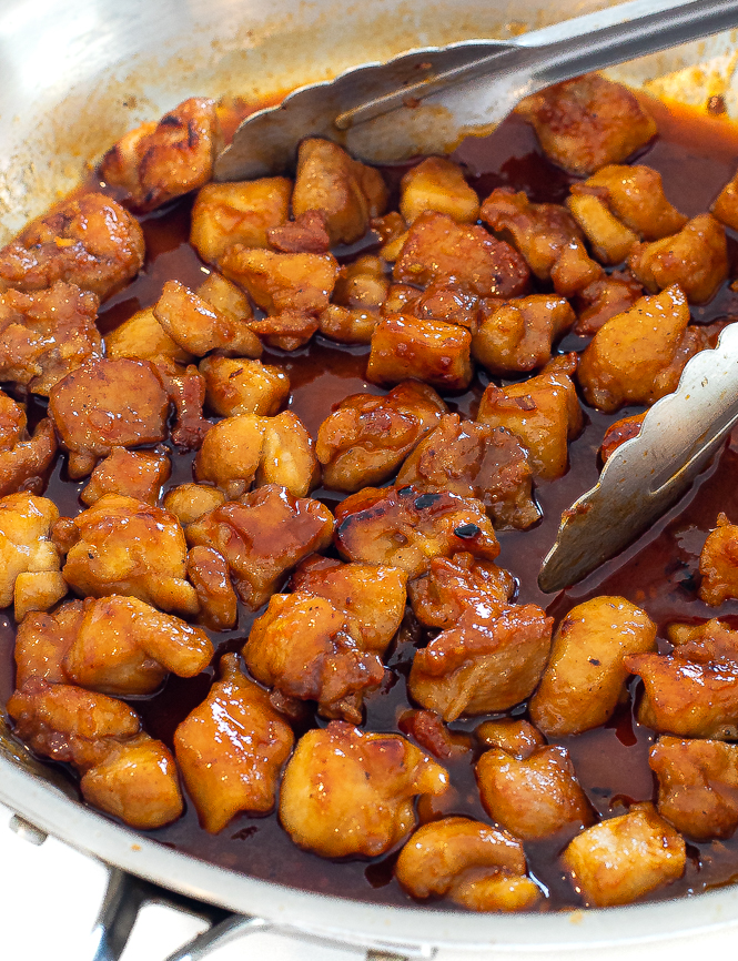 Firecracker chicken in a skillet with silver tongs. 