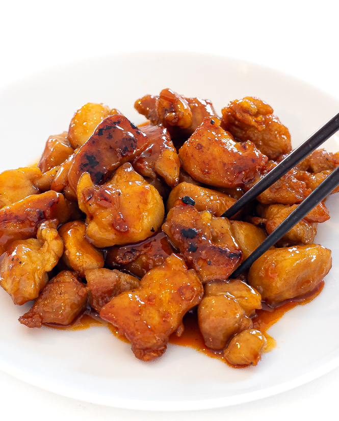 Firecracker chicken on a white plate with chopsticks.