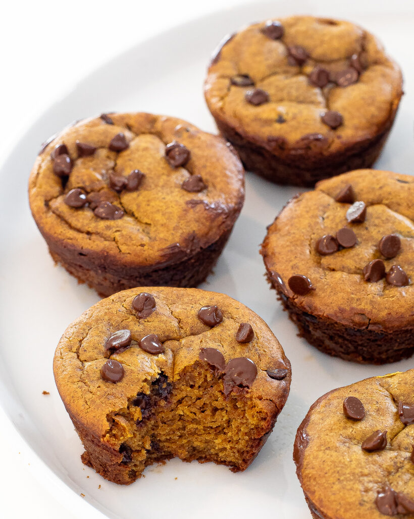 Flourless pumpkin muffins on a white plate with one muffin missing a bite.