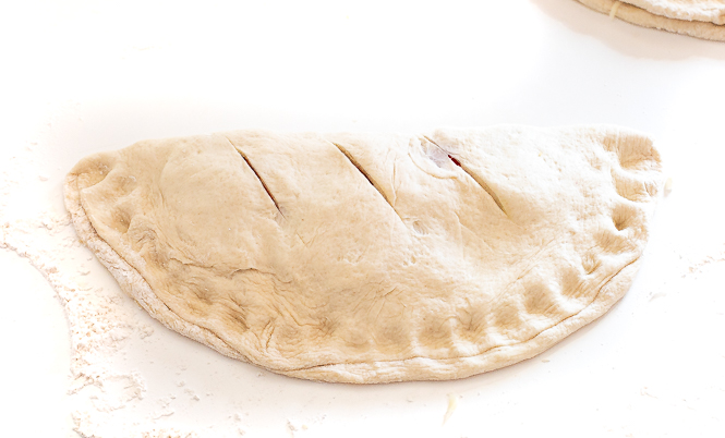 Raw calzone after being folded with three slits on the top.