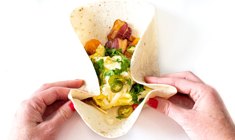 Hand folding up breakfast burrito.