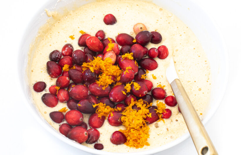 Fresh cranberries and orange zest in a bowl with the muffin batter and a spatula.