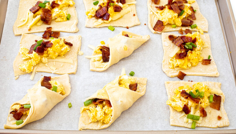 Folded puff pastry squares with toppings laid out on a baking sheet lined with parchment paper.