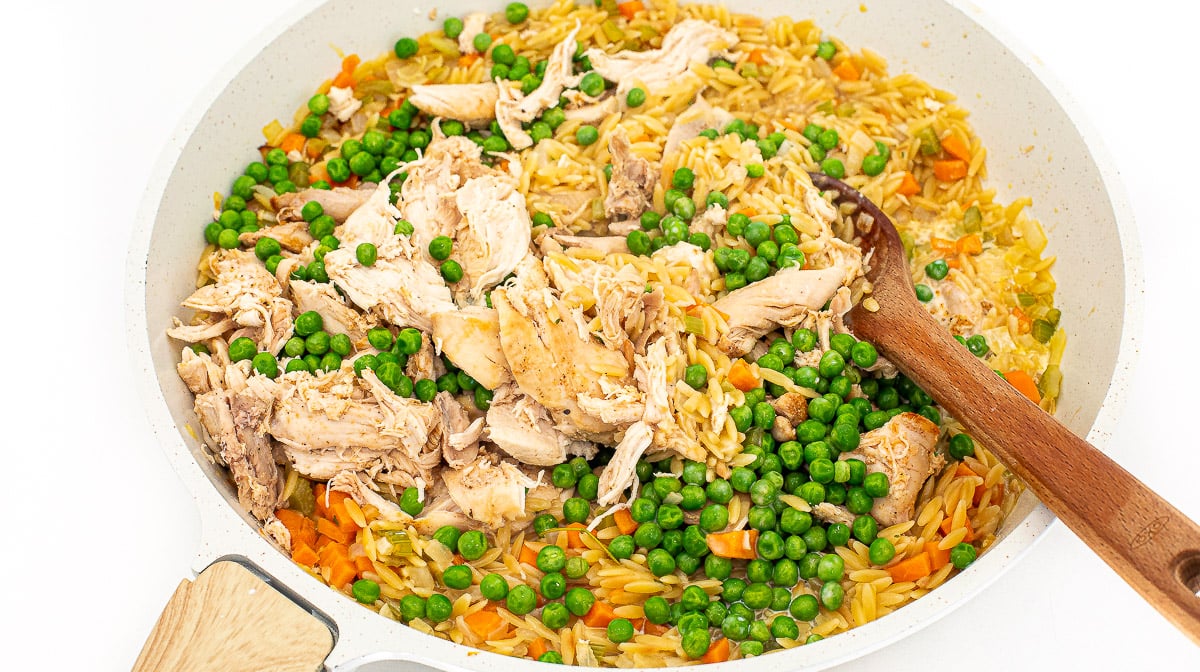 Stirring shredded chicken with orzo and veggies.
