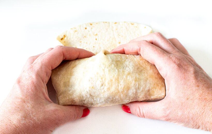 Hand folding up breakfast burrito.