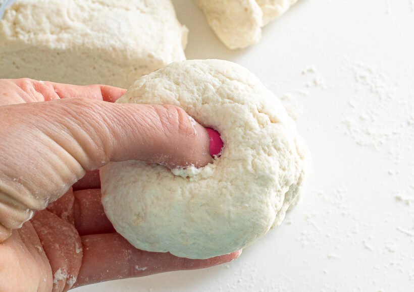 Finger poking a hole into the ball of bagel dough.
