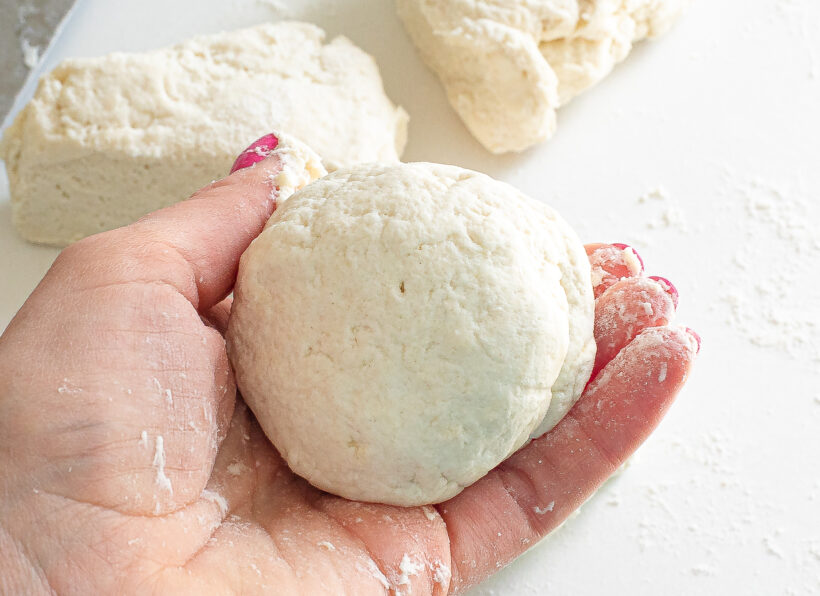 A hand holding a ball of bagel dough.