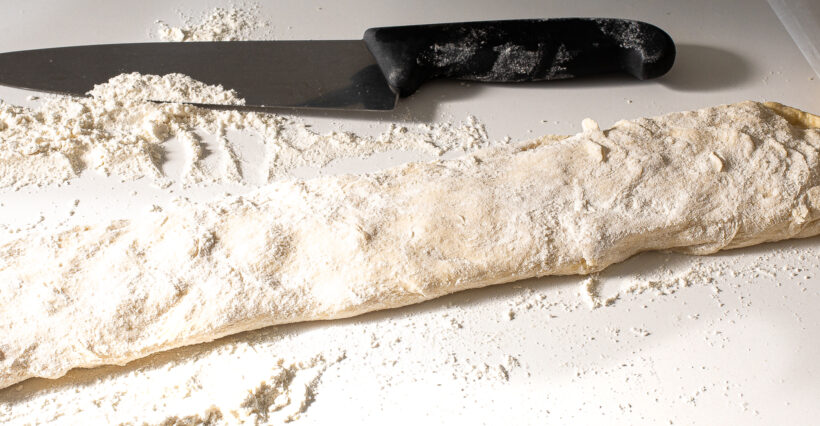 Dough on a floured surface next to a chef's knife.