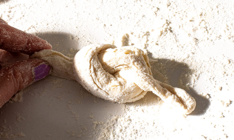 Hand holding knot of dough after it was tied in a knot.