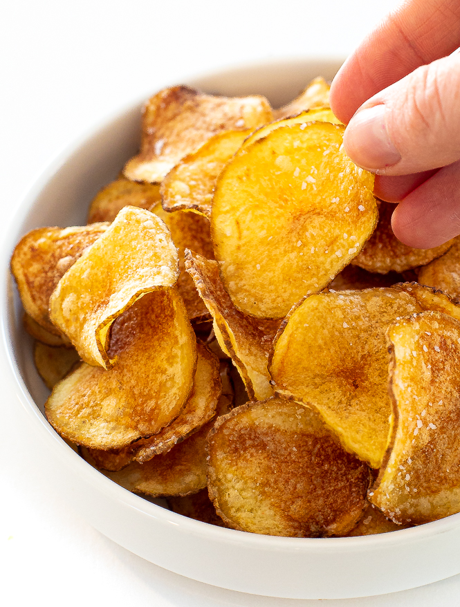 Hand picking up a potato chip out of a bowl filled with chips.