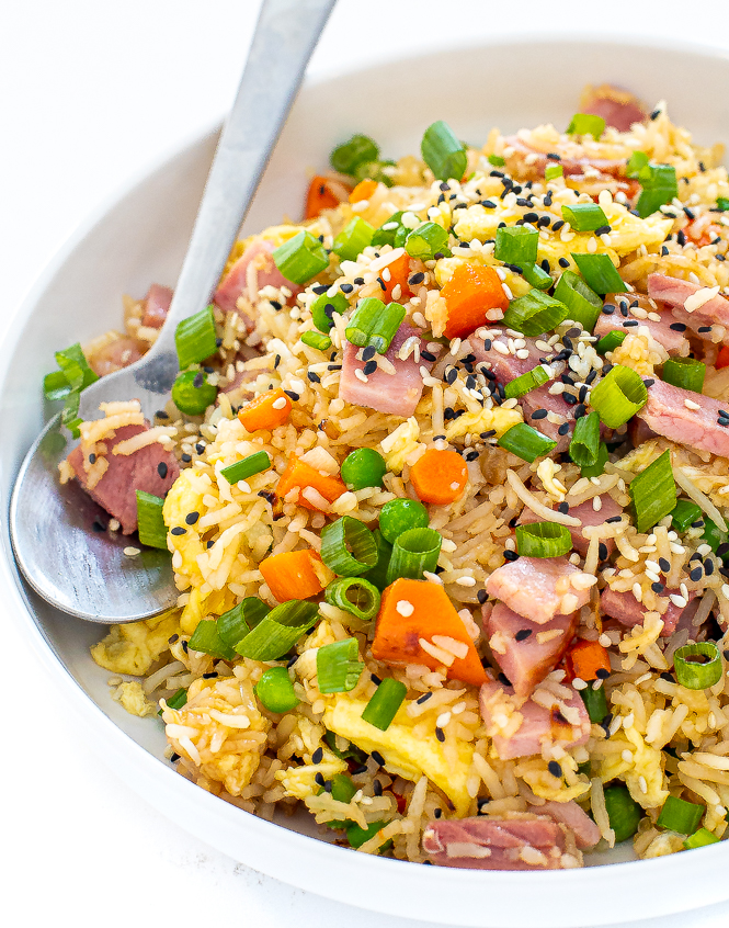 Rice with vegetables and ham in a white bowl with a silver spoon.