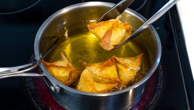Crab rangoons in a sauce pan filled with oil being fried. 