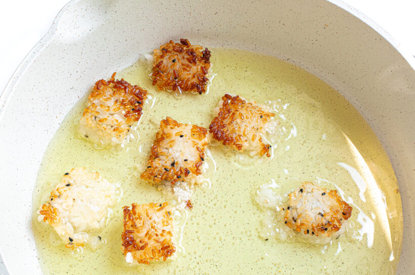 Sushi rice squares being fried in a skillet. 