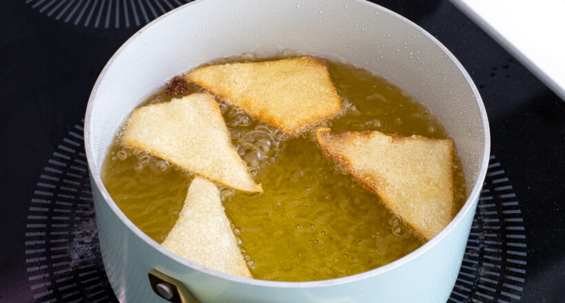 Wontons being fried in a pot of oil.