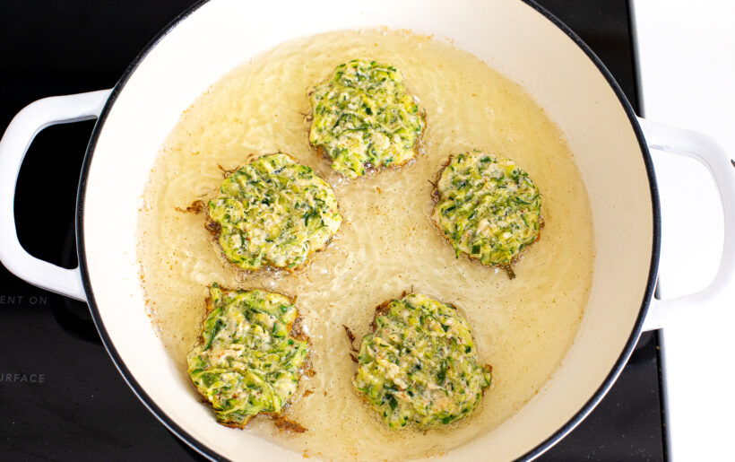 Zucchini fritters cooking in a pot of oil.
