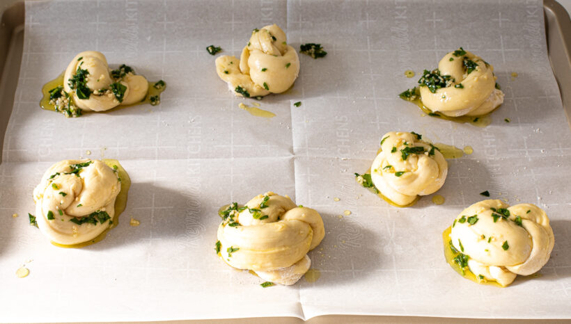 Dough knots on a baking sheet lined with parchment paper and brushed with garlic herb oil.