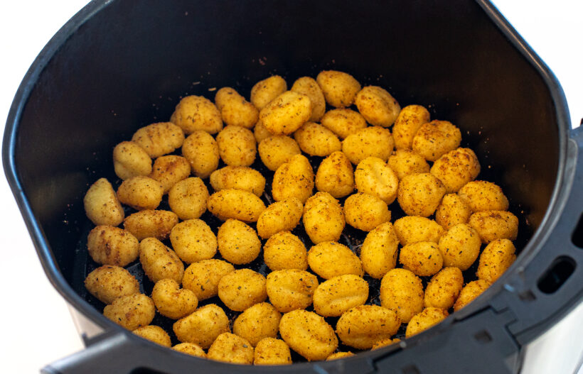 Gnocchi coated in spices in an air fryer basket.